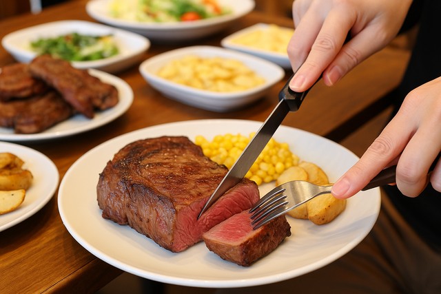 cutting-ribeye-steak-on-plate-with-corn-and-potatoes